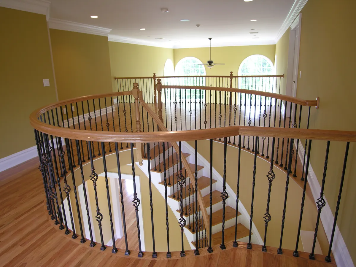Curved upper landing with wrought-iron balusters and a red oak handrail